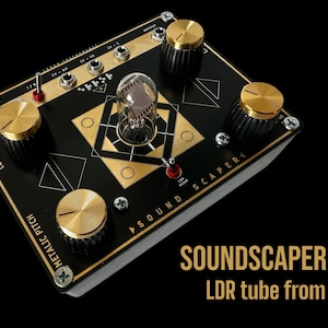May include: A gold-colored electronic music synthesizer with knobs and a vintage light-dependent resistor (LDR) tube. The device is labeled "SOUND SCAPER" and features a black and gold design.