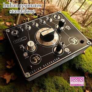 Puede incluir: Resonador indio negro independiente con perillas y diales plateados, y el símbolo Om. El dispositivo tiene el texto "Indian Resonator" y "Error Instruments". El fondo es musgo y follaje.