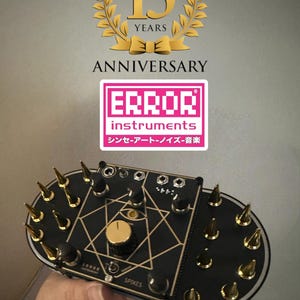 May include: A black electronic instrument with gold-colored spikes and knobs. The instrument has a geometric design and the text "ERROR INSTRUMENTS" and "SPIKES". The image also features a logo celebrating a 15-year anniversary.