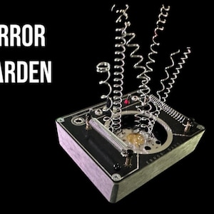 May include: A black box with the text "ERROR GARDEN" on it. The box has several silver springs attached to it, which are extended upwards.