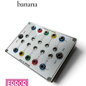 Op de afbeelding: Een rechthoekige Eurorack naar banaan modulaire synthesizer interface module met een zilveren voorplaat. Het bevat meerdere gekleurde in- en uitgangsaansluitingen gelabeld met cijfers en GND, vastgezet met vier schroeven in de hoeken.