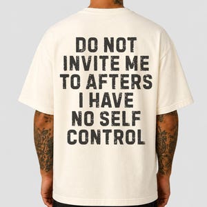 Könnte beinhalten: Ein cremefarbenes Kurzarm-T-Shirt mit schwarzem, verwaschen wirkendem Text auf der Rückseite: DO NOT INVITE ME TO AFTERS I HAVE NO SELF CONTROL. Das Shirt hat einen Rundhalsausschnitt und eine lockere Passform mit einem auffälligen Aufdruck.