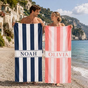 Puede incluir: Dos toallas de playa rectangulares con rayas verticales. Una toalla es azul marino y blanca con el nombre NOAH impreso en una banda horizontal central. La otra es rosa coral y blanca con el nombre OLIVIA en una banda horizontal central.