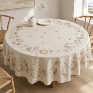 May include: A round, off-white tablecloth featuring a detailed, light brown printed pattern of various seashells and scattered small shell motifs. The design is arranged in a circular border around the edge and drapes over the sides of the table.
