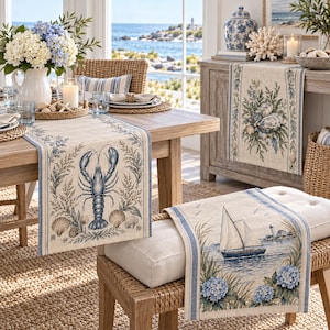 May include: A set of beige linen table runners featuring blue coastal-themed prints, including a lobster, a sailboat, and oyster shells, with blue border stripes and floral accents, displayed on a wooden dining table and a bench.