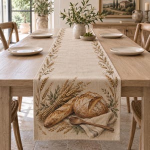 Puede incluir: Un camino de mesa de lino beige con un diseño estampado de tallos de trigo dorados, una hogaza de pan redonda, una barra de pan y una cuchara de madera sobre una servilleta de tela doblada, colocado sobre una mesa de comedor de madera con platos.