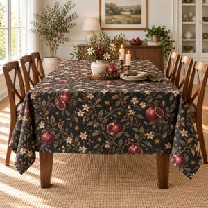 Könnte beinhalten: Eine rechteckige Tischdecke mit dunklem Hintergrund und einem wiederkehrenden Muster aus roten Granatäpfeln, weißen Blüten, grünen Blättern und kleinen goldenen Sternen. Der Stoff liegt auf einem hölzernen Esstisch mit vier Stühlen.