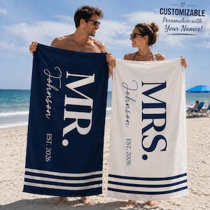 May include: Two rectangular beach towels featuring customizable text. One navy blue towel displays white text reading MR. Johnson EST. 2026, and one white towel displays navy text reading MRS. Johnson EST. 2026. Both towels have three horizontal stripes at the bottom.