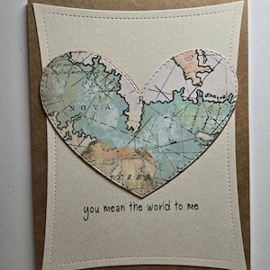 May include: A card with a heart-shaped world map in shades of blue, green, and brown. The text "you mean the world to me" is printed below the map.