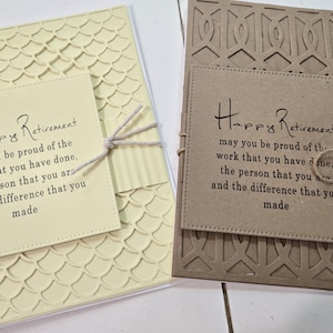 Peut inclure: Deux cartes de retraite faites &agrave; la main. L'une est de couleur cr&egrave;me avec un motif textur&eacute; et une &eacute;tiquette carr&eacute;e avec le texte "Happy Retirement". L'autre est marron avec un motif d&eacute;coup&eacute; d&eacute;coratif et une &eacute;tiquette similaire. Les deux cartes sont attach&eacute;es avec de la ficelle.