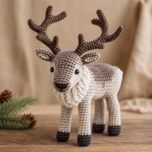 May include: A crochet reindeer toy featuring a light beige body, dark brown antlers, and a cream-colored textured neck ruff. The figure has black bead eyes, a dark brown stitched nose, and dark brown hooves on all four legs.