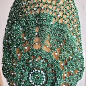 May include: Green crochet hair net with white beads. The net is made of a sparkly material and has a delicate pattern.