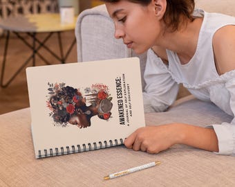 May include: A cream-colored spiral bound journal with the title "Awakened Essence: A Journal of Self Exploration and Self Discovery" printed on the cover. The cover features a colorful illustration of a woman with flowers in her hair.