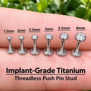 Op de afbeelding: Een set van zes schroefloze push-pin studs van implantaat-titanium met heldere edelstenen, variërend in grootte van 1,5 mm tot 4 mm. Elke stud heeft een platte achterkant en een ronde zetting, met de maten duidelijk aangegeven boven elk item.