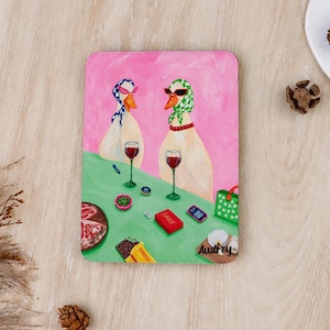 Könnte beinhalten: Ein rechteckiger Druck mit zwei Gänsen, die Kopftücher und Sonnenbrillen tragen und an einem grünen Tisch sitzen, mit Weingläsern, einer roten Schachtel mit der Aufschrift SASSY, einem Smartphone, einer Schokolade und dem Namen Audrey.