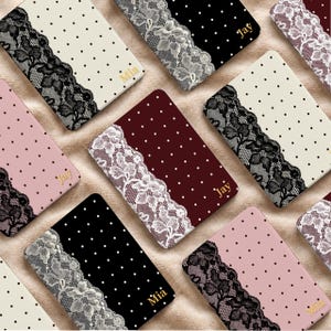 May include: A collection of rectangular notebooks featuring polka dot patterns in cream, black, burgundy, and pink. Each notebook is accented with a decorative lace trim along one side and includes a gold-colored name printed on the cover.