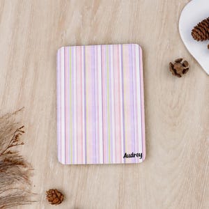 Könnte beinhalten: Ein rechteckiges Notizbuch mit vertikalem Streifenmuster in den Farben Hellrosa, Lavendel, Weiß und Limettengrün. Der Name Audrey ist in schwarzer Schreibschrift in der unteren rechten Ecke des Einbands mit abgerundeten Ecken aufgedruckt.