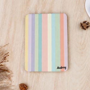 Könnte beinhalten: Eine rechteckige Tablethülle mit einem vertikalen Streifenmuster in Pastelltönen wie Gelb, Lila, Türkis, Rosa und Orange. Der Name Audrey ist in einer schwarzen Schreibschrift in der unteren rechten Ecke der Hülle aufgedruckt.