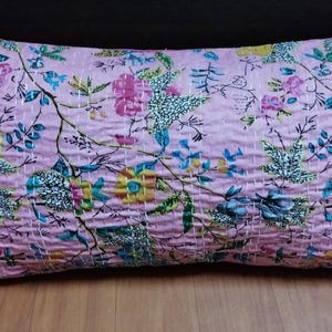 May include: A rectangular throw pillow featuring a light pink base color with a multi-colored floral and botanical print. The fabric surface displays visible white horizontal running stitch quilting patterns throughout the entire pillow cover.