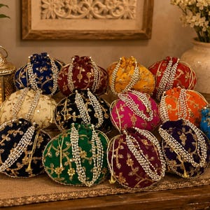 May include: A collection of round drawstring pouches in various colors including blue, red, yellow, green, and purple. Each pouch features intricate gold floral embroidery and is finished with a decorative white pearl beaded drawstring closure.