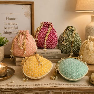 May include: A collection of six drawstring pouches in peach, magenta, dark green, cream, yellow, and mint green. Each pouch features intricate white floral embroidery and is finished with gold-toned drawstrings adorned with hanging pearl-like beads.