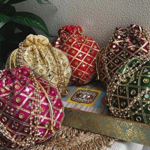 May include: Four drawstring pouches in magenta, cream, red, and dark green satin fabric. Each pouch features a gold lattice pattern, small circular mirrors, and gold embroidery. A long, delicate string of white faux pearls hangs from each bag.