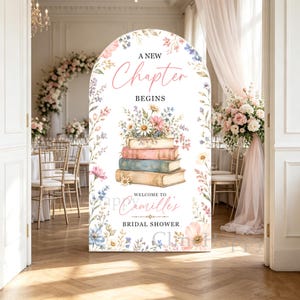 May include: An arched sign featuring a stack of three vintage books topped with a floral bouquet. The text reads A NEW Chapter BEGINS, WELCOME TO Camille's BRIDAL SHOWER. The design is framed by watercolor wildflowers in pink, blue, and green tones.