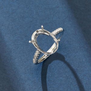 Peut inclure: Une monture de bague argentée dotée d'un support ovale à griffes conçu pour accueillir une pierre précieuse. L'anneau est orné d'une rangée de petites pierres claires et scintillantes incrustées le long de la tige, ajoutant une finition décorative.