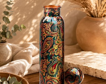 May include: A cylindrical copper water bottle featuring a vibrant, multi-colored paisley pattern in shades of teal, red, yellow, and green. The bottle has a narrow neck and a matching circular screw-top lid placed beside it on the surface.