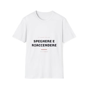 Puede incluir: Una camiseta blanca de manga corta con el texto IT SUPPORT HOTLINE en la parte superior, las palabras SPEGNERE E RIACCENDERE en letras negras grandes en el centro, una línea roja horizontal y el texto Lvl 1 support en la parte inferior.