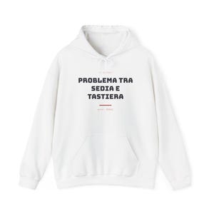 Op de afbeelding: Een witte hoodie met een kangoeroezak aan de voorzijde en lange mouwen. Op de borst staat de zwarte tekst "PROBLEMA TRA SEDIA E TASTIERA" met een kleine rode horizontale lijn eronder en aanvullende tekst boven en onder.