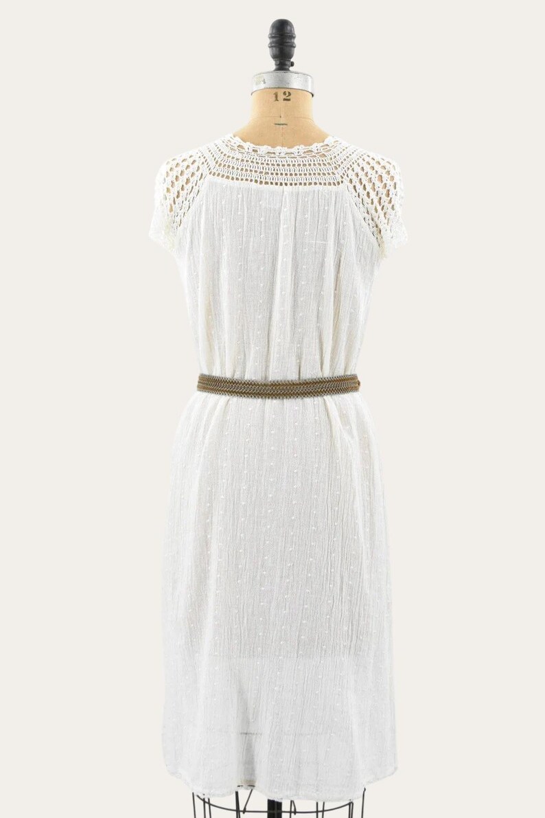 May include: A white, short-sleeved dress with a crochet neckline and a textured fabric. A brown belt cinches the waist. The dress is displayed on a mannequin.