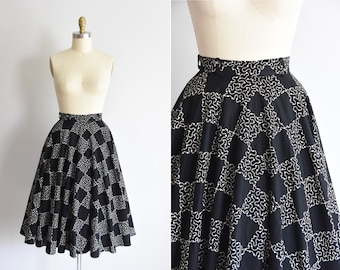 May include: A black and white patterned circle skirt with a high waist. The skirt has a white embroidered design on a black background.