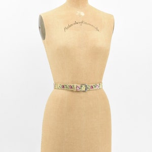 May include: A vintage floral patterned belt with a silver buckle on a dress form. The dress form is labeled "Palmenberg, Cavendish" and "Model 1953, 12".