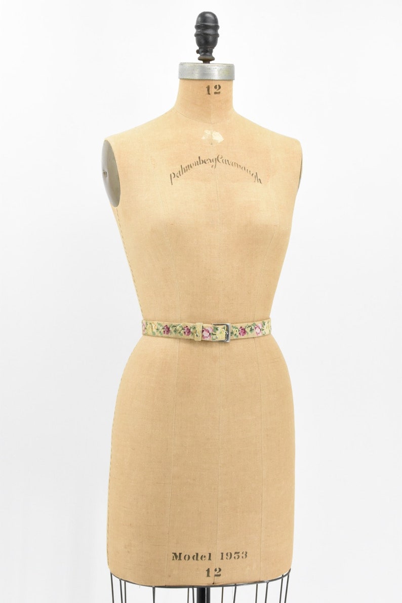 May include: A vintage floral patterned belt with a silver buckle on a dress form. The dress form is labeled "Palmenberg, Cavendish" and "Model 1953, 12".