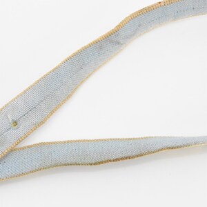 May include: A light blue ribbon with a tan trim. The ribbon is made of a woven fabric.