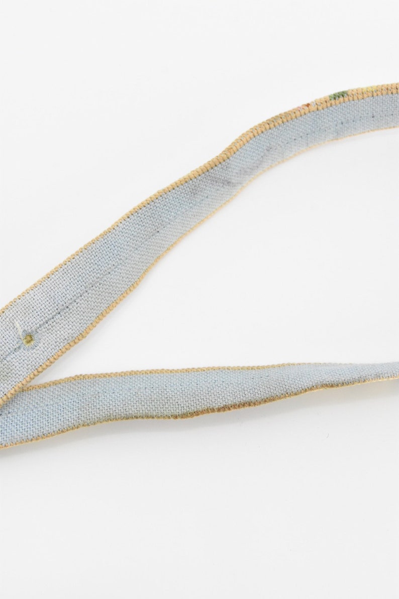 May include: A light blue ribbon with a tan trim. The ribbon is made of a woven fabric.