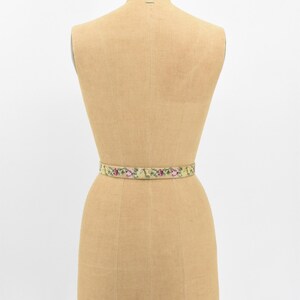 May include: A vintage floral embroidered belt in shades of green, yellow, and pink on a dress form.