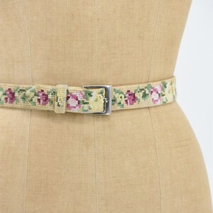 May include: A beige woven belt with a silver buckle and a floral pattern of pink, yellow, and green flowers.