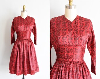 May include: A red dress with a black fish print. The dress has a fitted bodice and a full skirt. It has a belt at the waist.