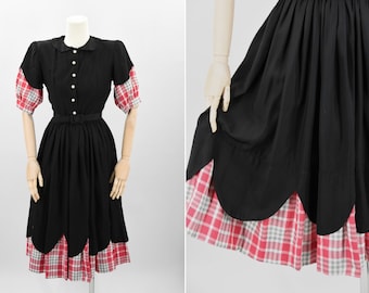May include: A black dress with a white collar and red and white plaid sleeves. The skirt has a scalloped hemline with a red and white plaid trim.