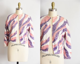May include: A pink, white, and purple sequined cropped jacket with a collapsible shoulder detail. The jacket has a zebra-like pattern.