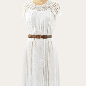 May include: A white vintage dress with a crochet neckline and short sleeves. The dress features a textured bodice and a brown belt cinching the waist. The dress is displayed on a mannequin.