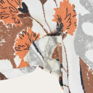 May include: Close-up of a fabric with a floral pattern. The design features orange, brown, and gray flowers on a white background. The fabric appears to be soft and possibly used for clothing or home decor.