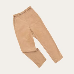 May include: Tan-colored pants with a matching belt. The pants have a straight leg design and a classic, neutral color. The belt has a silver-colored buckle. The pants are made of a soft, possibly suede-like material.