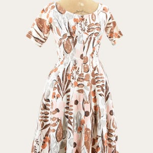 May include: A vintage white dress with a floral pattern in shades of brown, orange, and pink. The dress features short sleeves and a fitted bodice that flares into a full skirt. The dress is displayed on a mannequin.