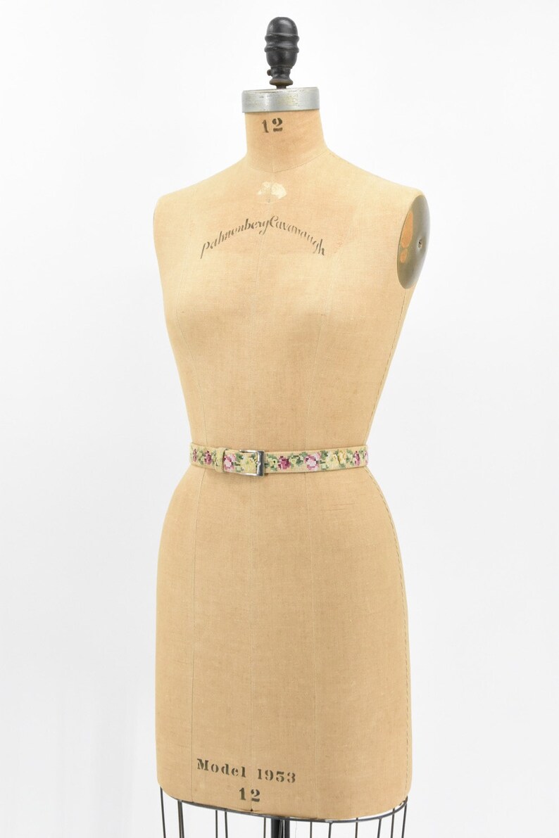 May include: A vintage dress form with a floral patterned belt. The dress form is made of tan fabric and has a label that reads "Pellham & Kay, Norwich".