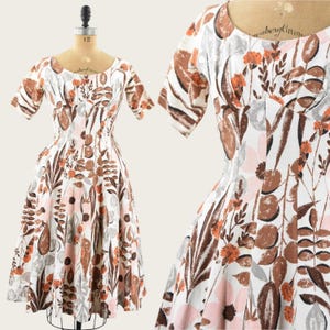 May include: A vintage white dress with a scoop neckline and short sleeves. The dress features a floral pattern in shades of brown, orange, and pink. The dress is displayed on a mannequin.