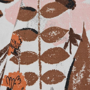 May include: Close-up of a fabric with a floral pattern. The design features brown, orange, and black floral and leaf motifs against a white background. Pink, gray, and brown shapes are also present, creating a textured look.