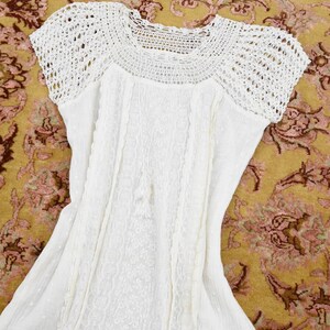 May include: White dress with a crochet yoke and short sleeves. The dress features detailed embroidery and a flowing skirt. The garment is made of a lightweight fabric, perfect for warm weather. The dress is laid out on a patterned rug.
